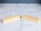 Two light natural wood rectangular blocks with grooved slots, placed on a white marble surface against a dark blue-gray background.